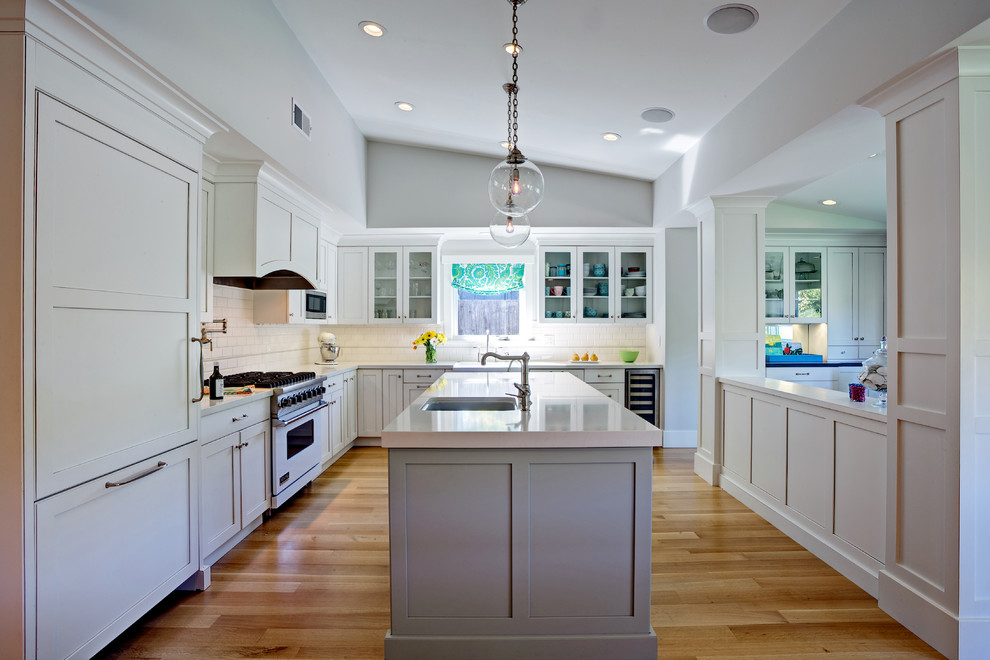 Mid-sized transitional l-shaped open plan kitchen in San Francisco with a farmhouse sink, shaker cabinets, white cabinets, quartz benchtops, white splashback, ceramic splashback, stainless steel appliances, medium hardwood floors and with island.