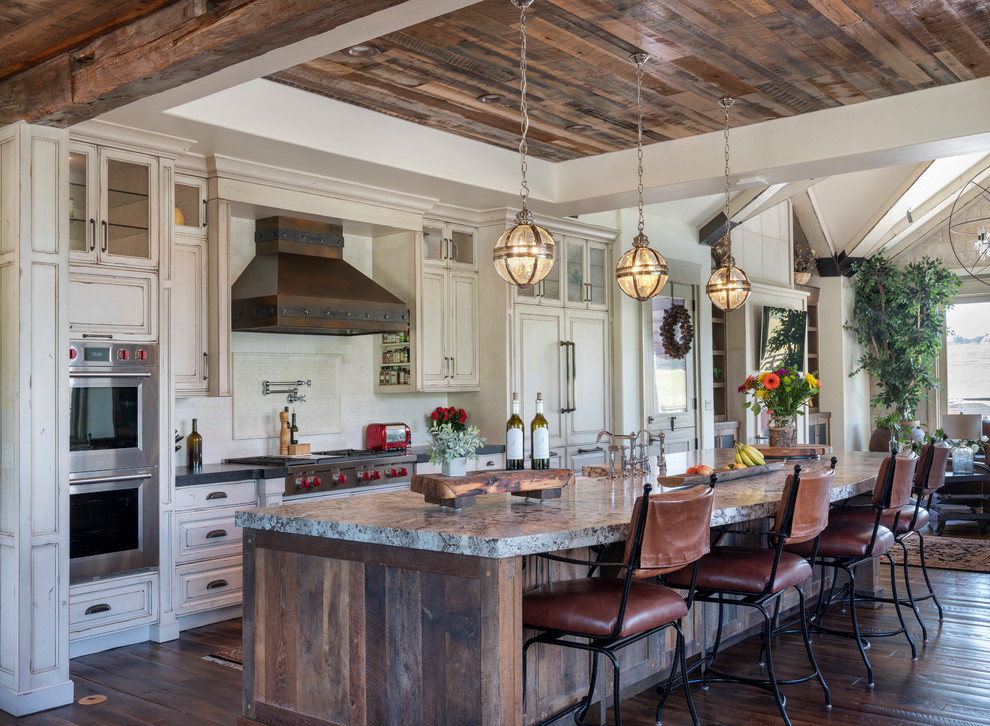 Country galley kitchen in Denver with raised-panel cabinets, distressed cabinets, white splashback, stainless steel appliances, dark hardwood floors, with island, brown floor and grey benchtop.