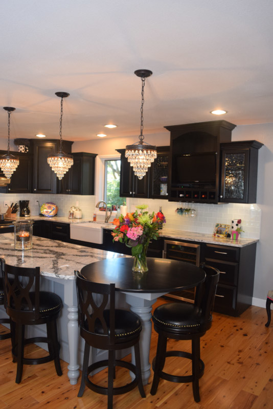 Inspiration for a transitional medium tone wood floor kitchen remodel in Chicago with a farmhouse sink, raised-panel cabinets, black cabinets, quartz countertops, white backsplash, glass tile backsplash, stainless steel appliances and an island