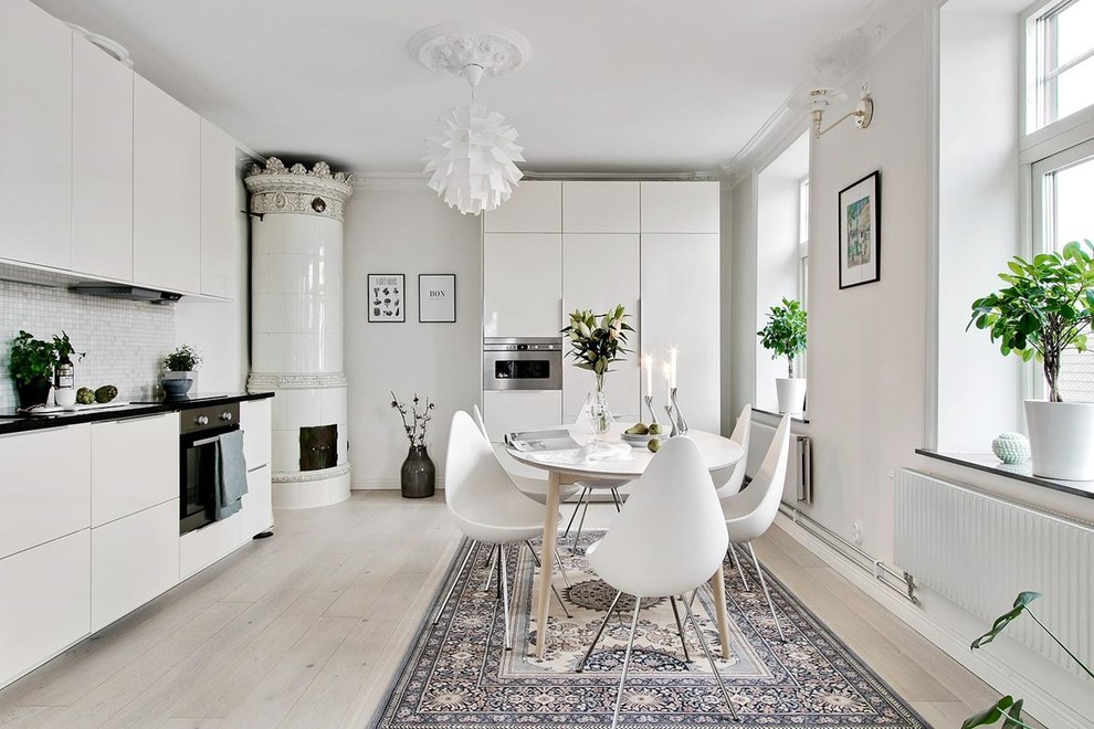 Inspiration for a mid-sized scandinavian l-shaped eat-in kitchen in Other with flat-panel cabinets, white cabinets, mosaic tile splashback, panelled appliances, light hardwood floors, no island, white splashback and white floor.
