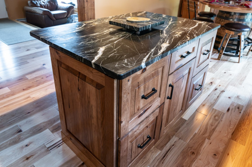 Inspiration for a rustic l-shaped medium tone wood floor kitchen remodel in Boston with an undermount sink, raised-panel cabinets, medium tone wood cabinets, granite countertops, gray backsplash, stainless steel appliances, an island and black countertops