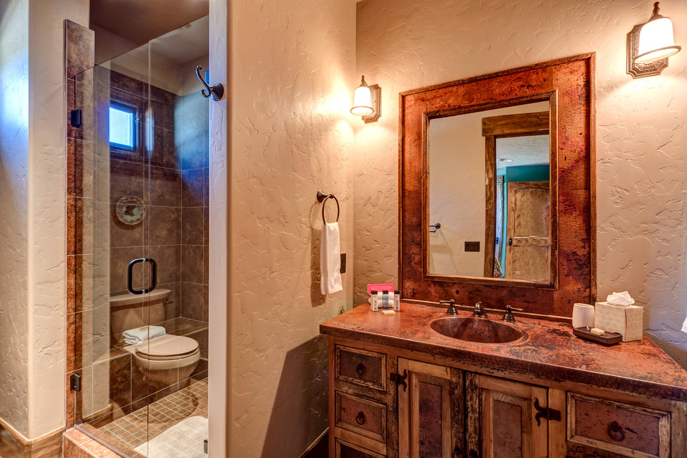 This is an example of a mid-sized country bathroom in Denver with louvered cabinets, distressed cabinets, a drop-in tub, a corner shower, a two-piece toilet, beige tile, brown tile, limestone, beige walls, limestone floors, an undermount sink, multi-coloured floor, a hinged shower door, copper benchtops and orange benchtops.