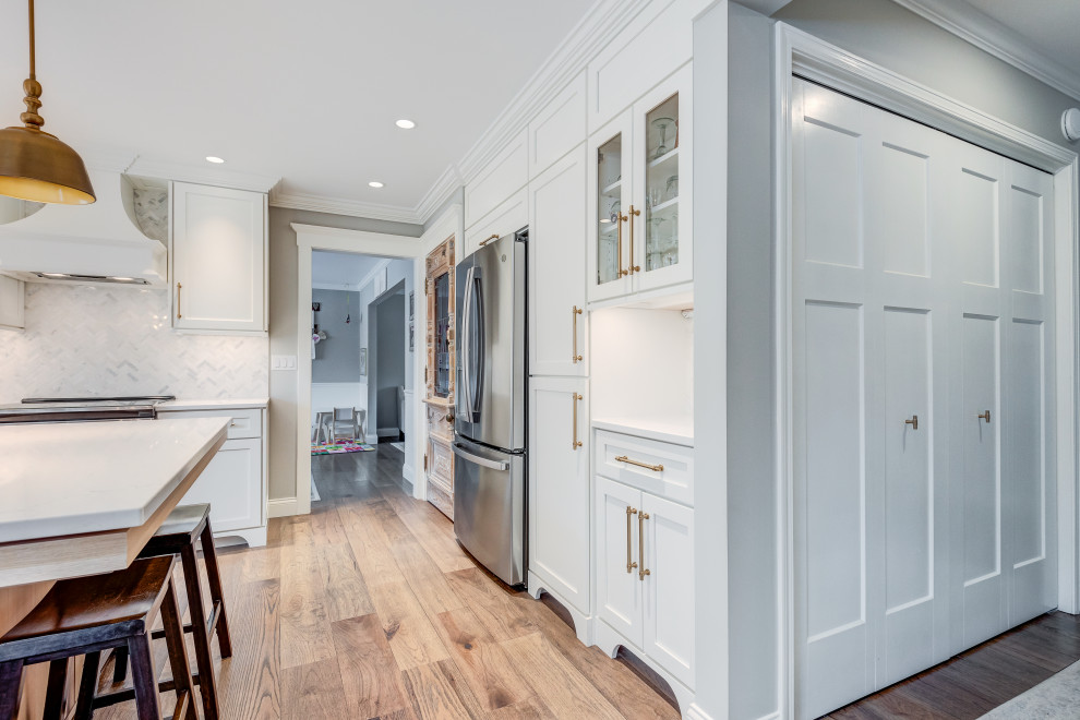 Design ideas for a mid-sized transitional l-shaped eat-in kitchen in Chicago with a farmhouse sink, shaker cabinets, white cabinets, quartzite benchtops, white splashback, glass tile splashback, coloured appliances, light hardwood floors, with island, brown floor and white benchtop.