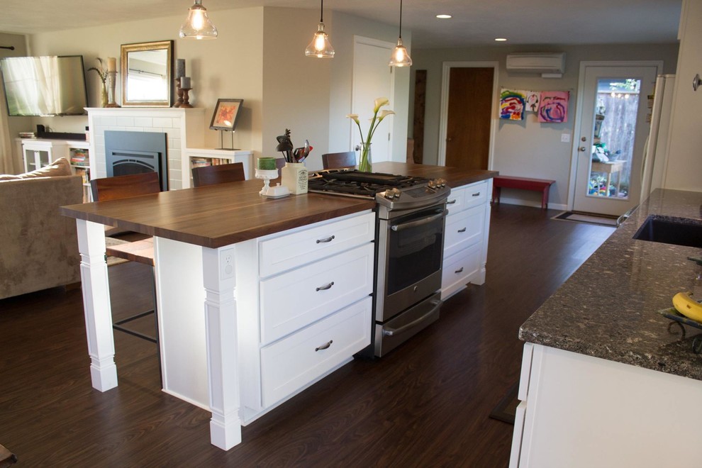Example of a mid-sized transitional l-shaped dark wood floor and brown floor open concept kitchen design with an undermount sink, shaker cabinets, white cabinets, wood countertops, white backsplash, porcelain backsplash, white appliances and an island