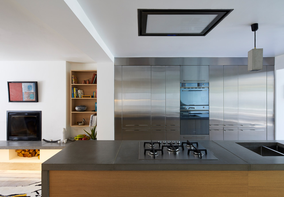 Mid-sized modern kitchen in London with flat-panel cabinets, stainless steel cabinets, concrete benchtops, light hardwood floors, with island and beige floor.