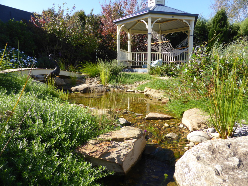 This is an example of a country backyard garden in Other with a water feature.