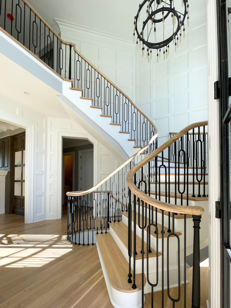 Imagen de escalera curva clásica renovada extra grande con escalones de madera, contrahuellas de madera, barandilla de varios materiales y boiserie