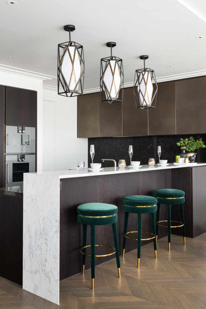 This is an example of a contemporary u-shaped kitchen in London with flat-panel cabinets, brown cabinets, black splashback, stone slab splashback, stainless steel appliances, dark hardwood floors, a peninsula, brown floor and white benchtop.