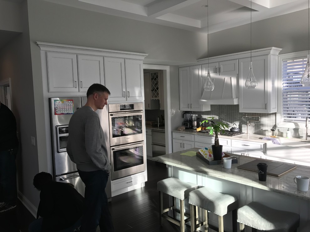 Example of a large transitional l-shaped light wood floor and multicolored floor eat-in kitchen design in Chicago with beaded inset cabinets, white cabinets, quartz countertops, black backsplash, ceramic backsplash, stainless steel appliances and an island