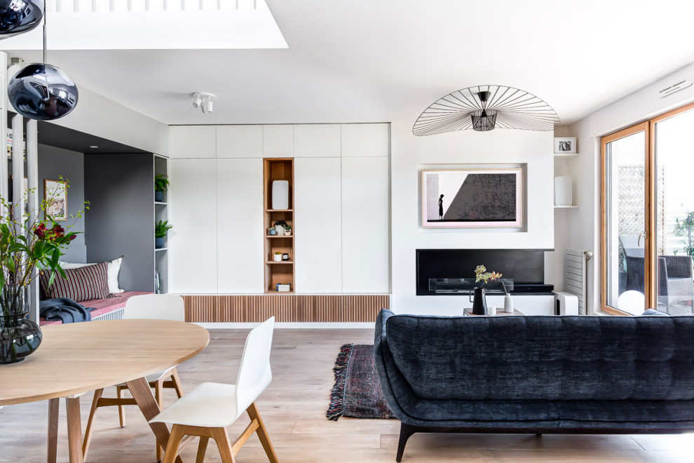 Photo of a large modern open concept family room in Paris with white walls, a corner fireplace, a wall-mounted tv, a library and light hardwood floors.