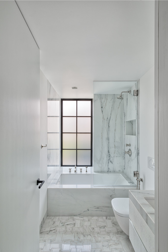 Inspiration for a small contemporary 3/4 bathroom in New York with white cabinets, an alcove tub, a wall-mount toilet, white tile, stone slab, white walls, terrazzo floors, an undermount sink, terrazzo benchtops, white floor and white benchtops.