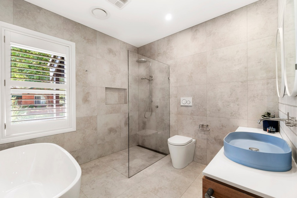 This is an example of a modern 3/4 bathroom in Melbourne with medium wood cabinets, a freestanding tub, a corner shower, a wall-mount toilet, white tile, ceramic tile, ceramic floors, engineered quartz benchtops, an open shower, white benchtops, a single vanity and a floating vanity.