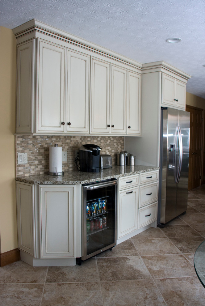 Example of a large u-shaped ceramic tile eat-in kitchen design with a farmhouse sink, recessed-panel cabinets, distressed cabinets, granite countertops, beige backsplash, stone tile backsplash, stainless steel appliances and an island
