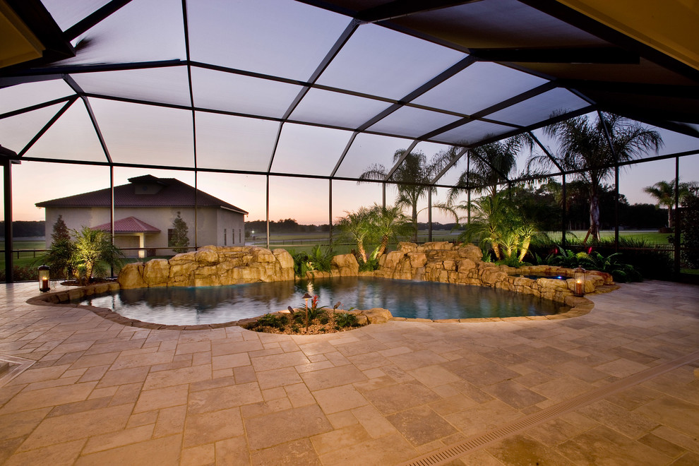 Photo of a mid-sized tropical backyard custom-shaped pool in Orlando with natural stone pavers and a hot tub.