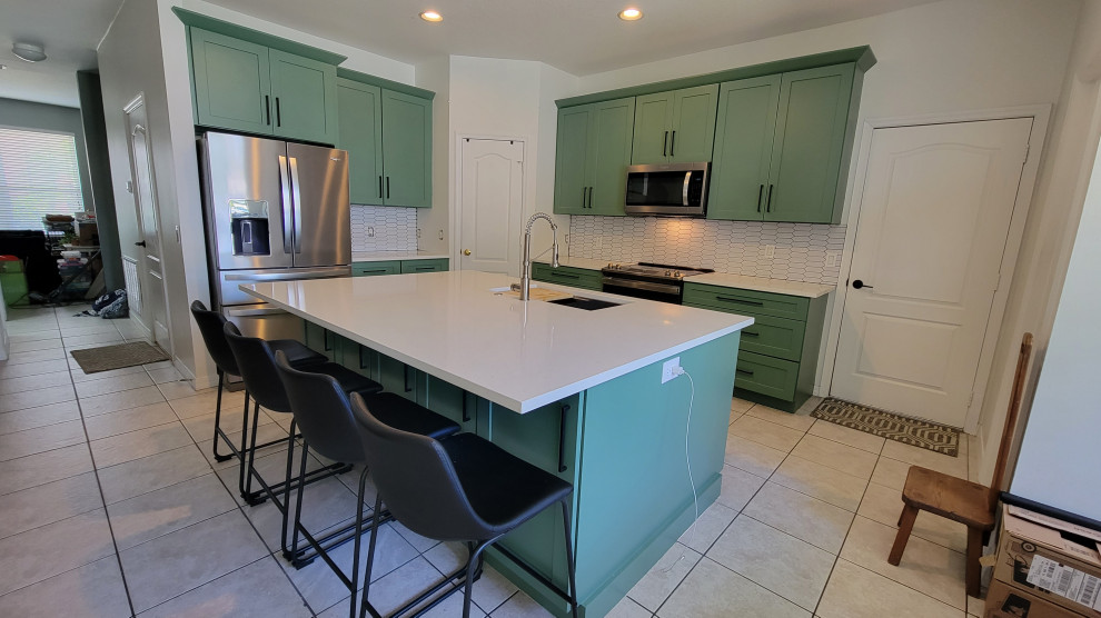Example of a mid-sized transitional l-shaped eat-in kitchen design in Orlando with shaker cabinets, green cabinets, quartz countertops, white backsplash, subway tile backsplash, an island and white countertops
