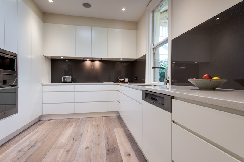 Design ideas for a mid-sized modern l-shaped eat-in kitchen in Other with an undermount sink, white cabinets, brown splashback, glass sheet splashback, stainless steel appliances and porcelain floors.