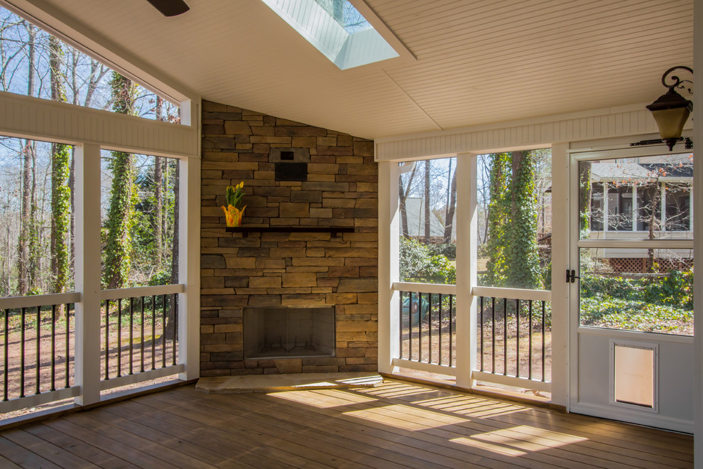 This is an example of a large country sunroom in Atlanta with medium hardwood floors, a standard fireplace, a stone fireplace surround and a skylight.