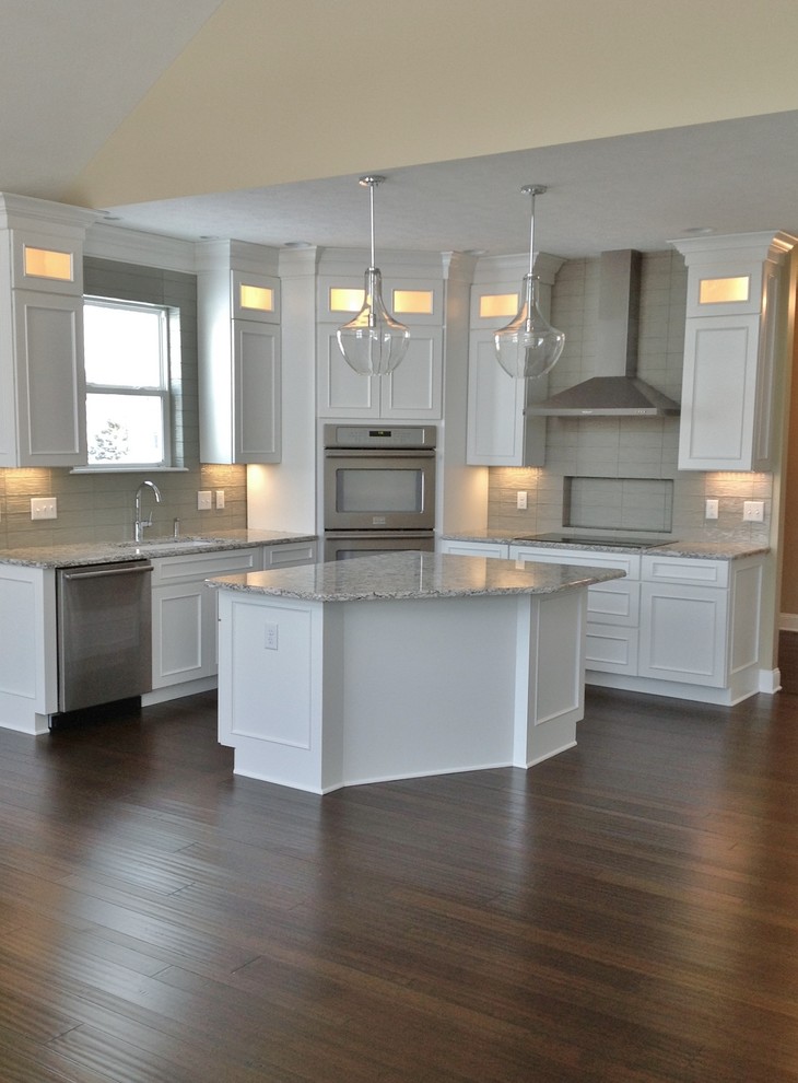 Mid-sized contemporary l-shaped eat-in kitchen in Cleveland with an undermount sink, recessed-panel cabinets, white cabinets, granite benchtops, grey splashback, cement tile splashback, stainless steel appliances, medium hardwood floors and with island.