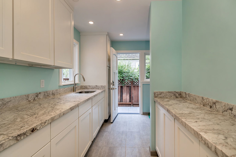 This is an example of an expansive contemporary galley utility room in San Francisco with an undermount sink, shaker cabinets, white cabinets, marble benchtops, green walls, porcelain floors, a side-by-side washer and dryer, grey floor and grey benchtop.