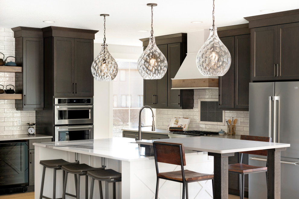 Inspiration for a transitional l-shaped kitchen in Minneapolis with shaker cabinets, dark wood cabinets, white splashback, stainless steel appliances, medium hardwood floors, with island, brown floor and white benchtop.