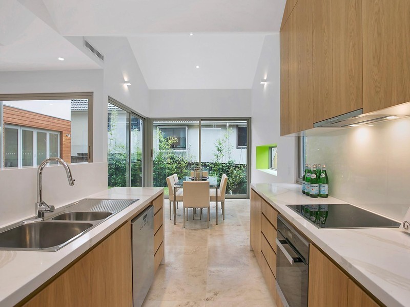 Photo of a contemporary u-shaped eat-in kitchen in Sydney with a double-bowl sink, raised-panel cabinets, brown cabinets, laminate benchtops, white splashback, glass sheet splashback, black appliances, ceramic floors and with island.