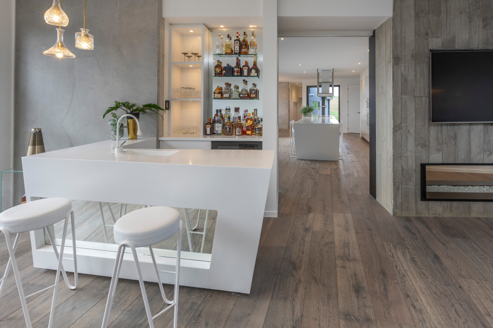 This is an example of a large contemporary galley seated home bar in Auckland with an undermount sink, flat-panel cabinets, white cabinets, solid surface benchtops, mirror splashback, medium hardwood floors, brown floor and yellow benchtop.