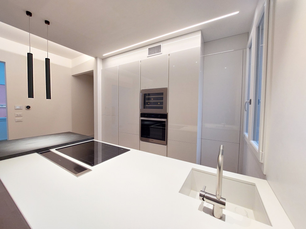 Example of a small trendy galley medium tone wood floor, beige floor and tray ceiling open concept kitchen design in Bologna with an integrated sink, flat-panel cabinets, white cabinets, solid surface countertops, a peninsula and white countertops
