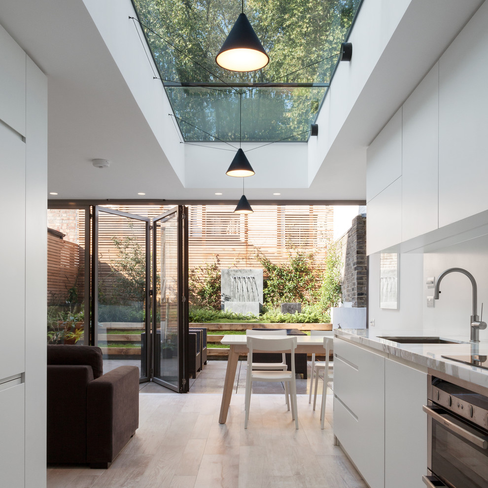 Photo of a contemporary galley open plan kitchen in London with a single-bowl sink, flat-panel cabinets, white cabinets, onyx benchtops, white splashback, stainless steel appliances, ceramic floors and no island.