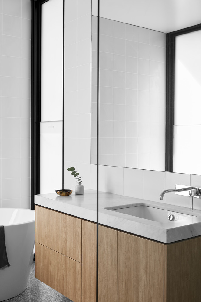Photo of a large contemporary kids bathroom in Melbourne with furniture-like cabinets, light wood cabinets, a freestanding tub, an alcove shower, a wall-mount toilet, white tile, ceramic tile, white walls, porcelain floors, an undermount sink, engineered quartz benchtops, grey floor, a hinged shower door and white benchtops.