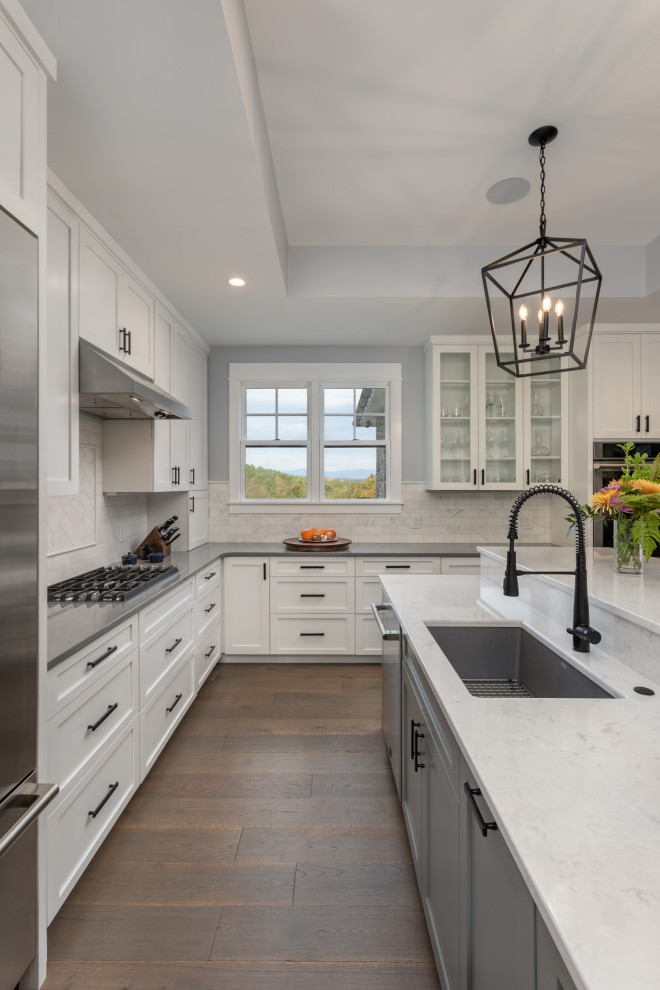 Foto på ett mellanstort vintage grå kök, med en undermonterad diskho, skåp i shakerstil, vita skåp, bänkskiva i kvarts, vitt stänkskydd, stänkskydd i marmor, rostfria vitvaror, mellanmörkt trägolv, en köksö och brunt golv