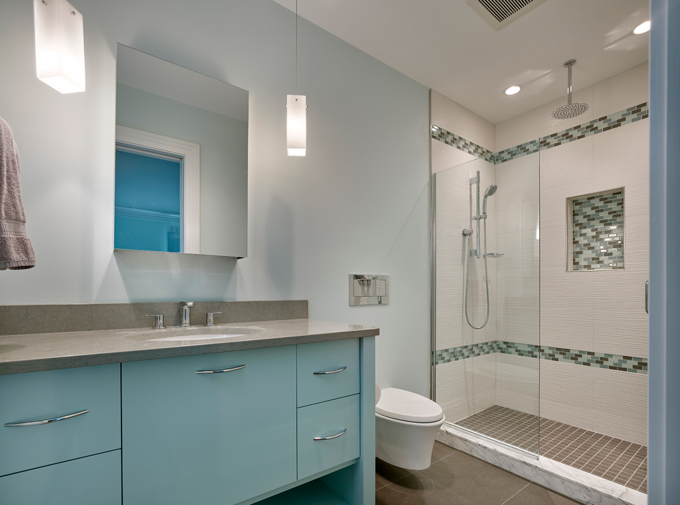 This is an example of a mid-sized beach style 3/4 bathroom in Wilmington with flat-panel cabinets, blue cabinets, an alcove shower, a wall-mount toilet, white tile, ceramic tile, blue walls, porcelain floors, an undermount sink, brown floor and a hinged shower door.