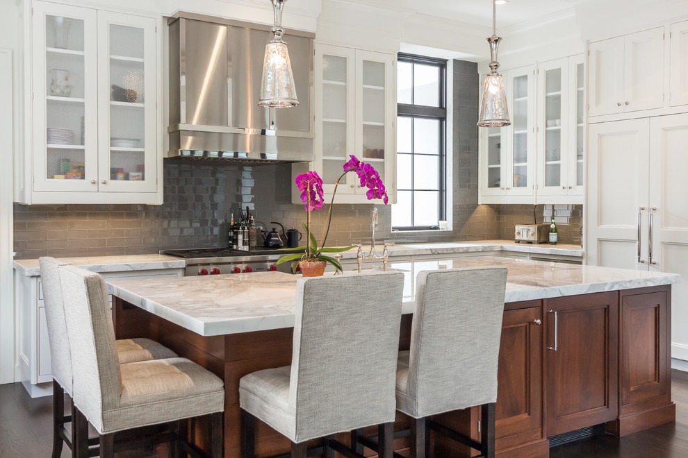 This is an example of a large transitional u-shaped kitchen in Other with a farmhouse sink, white cabinets, marble benchtops, grey splashback, subway tile splashback, stainless steel appliances, dark hardwood floors and with island.
