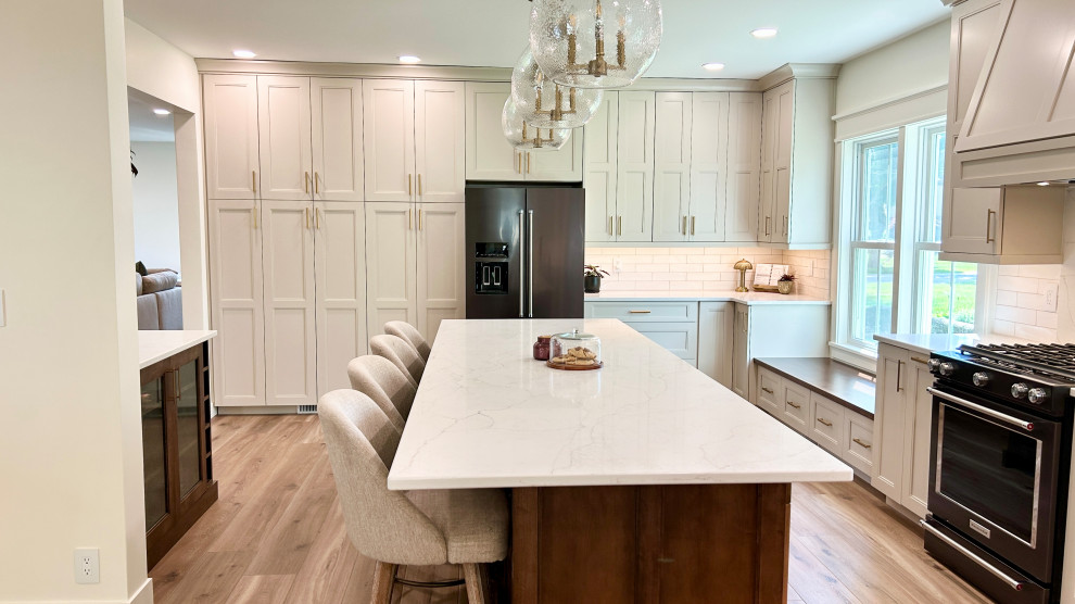 Large transitional u-shaped light wood floor open concept kitchen photo with an undermount sink, flat-panel cabinets, white cabinets, quartz countertops, white backsplash, ceramic backsplash, black appliances, an island and white countertops