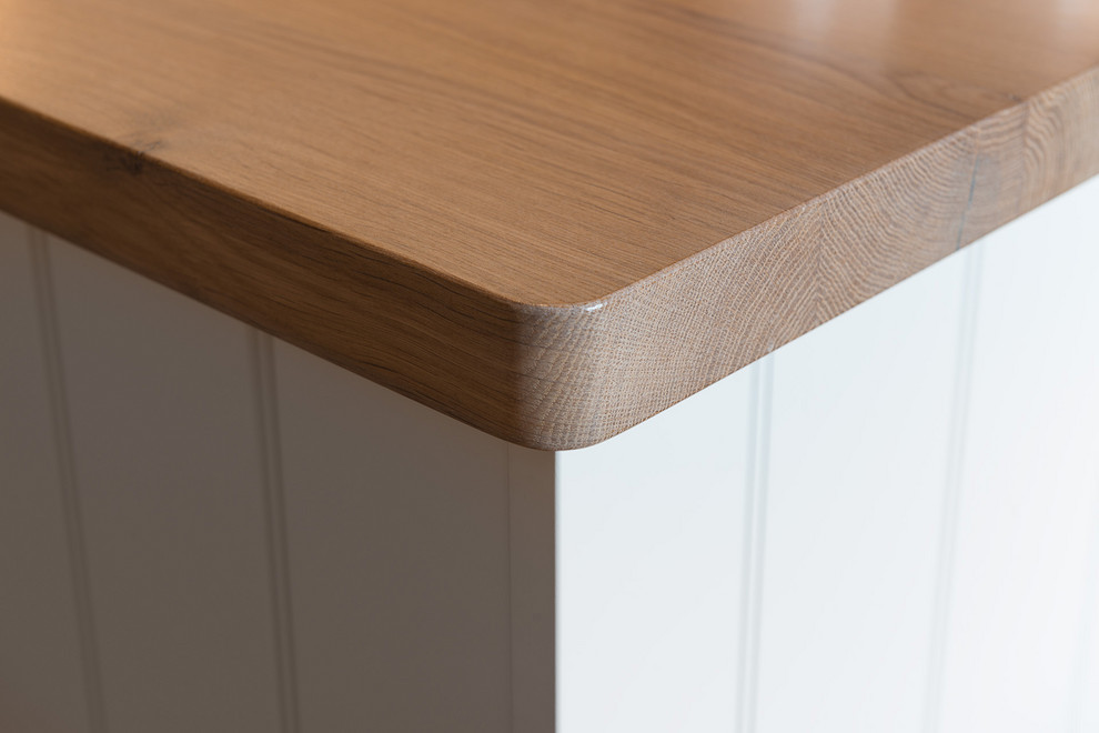 Wohnküche mit Landhausspüle, Lamellenschränken, weißen Schränken, Arbeitsplatte aus Holz, weißen Elektrogeräten, braunem Holzboden, Halbinsel, braunem Boden und brauner Arbeitsplatte in Munich