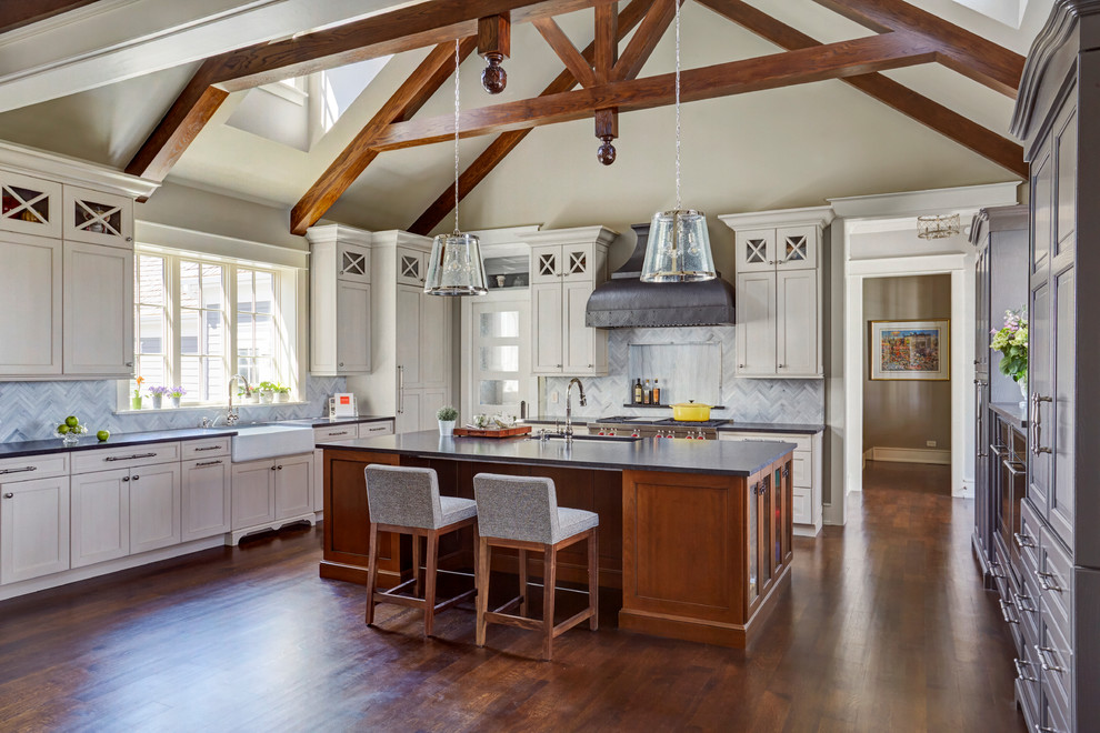 Inspiration for an expansive traditional galley open plan kitchen in Chicago with a farmhouse sink, shaker cabinets, white cabinets, granite benchtops, grey splashback, stone tile splashback, stainless steel appliances, dark hardwood floors, with island, brown floor and black benchtop.