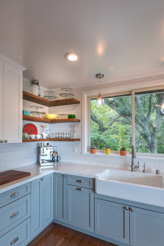 Photo of a mid-sized country eat-in kitchen in San Francisco with a farmhouse sink, shaker cabinets, white cabinets, white splashback, ceramic splashback, medium hardwood floors and no island.