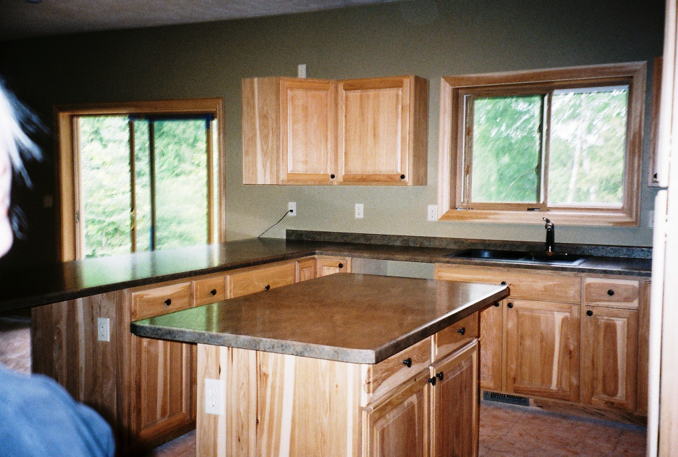 Mid-sized u-shaped laminate floor and brown floor eat-in kitchen photo with a double-bowl sink, raised-panel cabinets, beige cabinets, laminate countertops, black backsplash, stainless steel appliances, an island and black countertops
