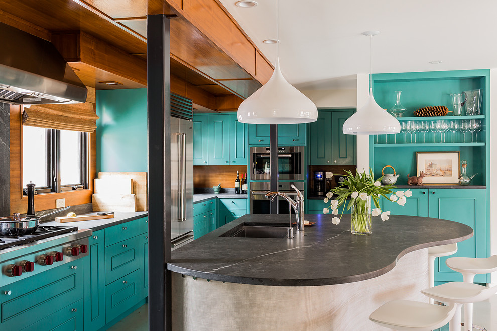 This is an example of a large eclectic galley eat-in kitchen in Boston with an undermount sink, beaded inset cabinets, blue cabinets, stainless steel appliances, with island, soapstone benchtops, brown splashback, timber splashback and black benchtop.