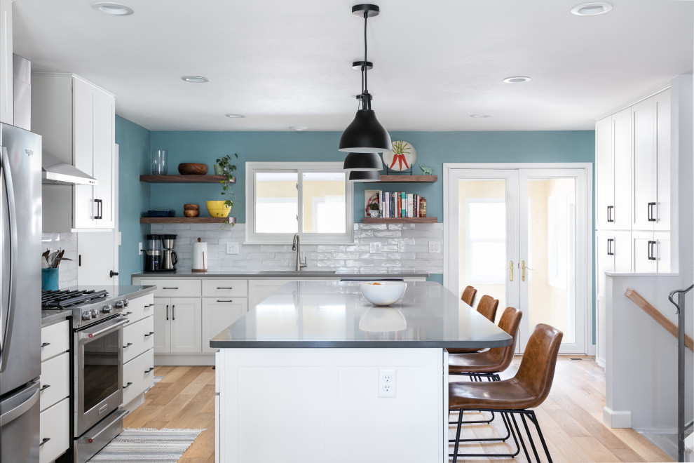 Eat-in kitchen - mid-sized transitional l-shaped light wood floor and brown floor eat-in kitchen idea in Denver with an undermount sink, shaker cabinets, white cabinets, quartz countertops, white backsplash, porcelain backsplash, stainless steel appliances, an island and gray countertops