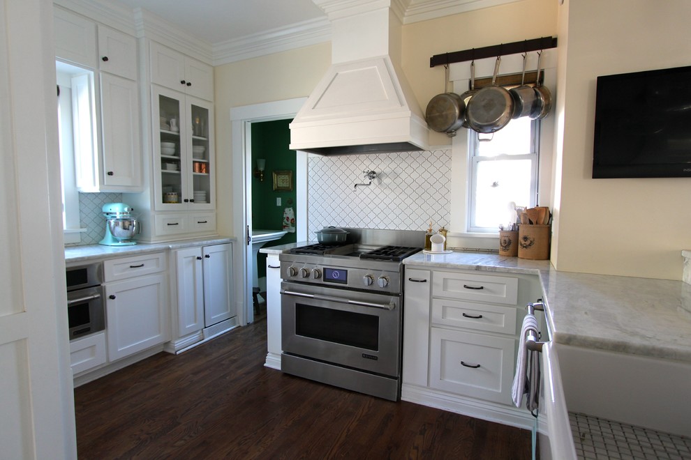 Example of a transitional medium tone wood floor kitchen design in Omaha with a farmhouse sink, shaker cabinets, white cabinets, quartzite countertops, white backsplash, ceramic backsplash, stainless steel appliances and a peninsula