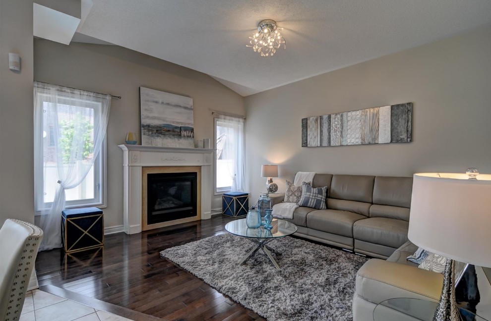 This is an example of a mid-sized transitional open concept family room in Toronto with beige walls, medium hardwood floors, a standard fireplace, a tile fireplace surround and brown floor.