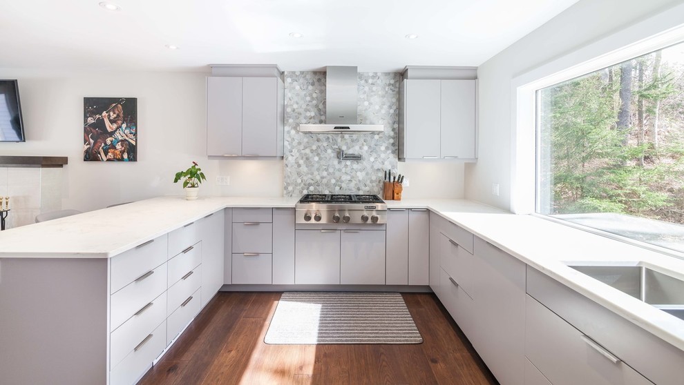 Example of a large minimalist u-shaped dark wood floor and brown floor eat-in kitchen design with a double-bowl sink, flat-panel cabinets, gray cabinets, quartzite countertops, gray backsplash, stone tile backsplash, stainless steel appliances and a peninsula