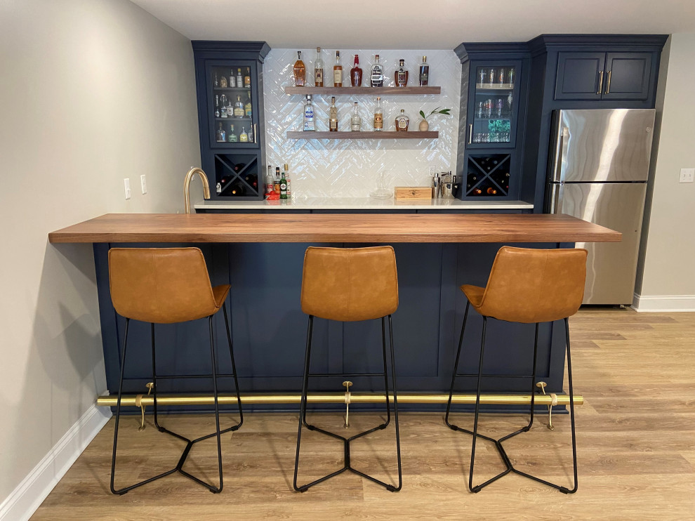 This is an example of a mid-sized transitional galley wet bar in Other with an undermount sink, blue cabinets, quartz benchtops, white splashback, subway tile splashback, dark hardwood floors, brown floor and white benchtop.