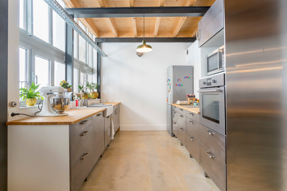 Large industrial galley separate kitchen in Lyon with a farmhouse sink, flat-panel cabinets, stainless steel cabinets, stainless steel appliances, no island and wood benchtops.