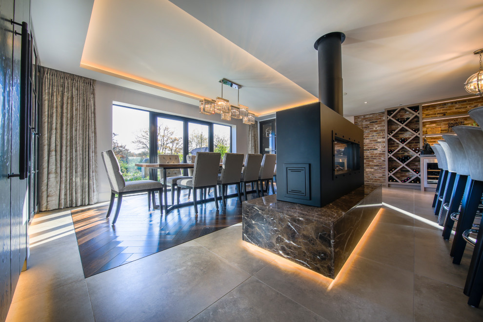 This is an example of a large contemporary kitchen/dining combo in Hampshire with ceramic floors, a two-sided fireplace, a stone fireplace surround and beige floor.