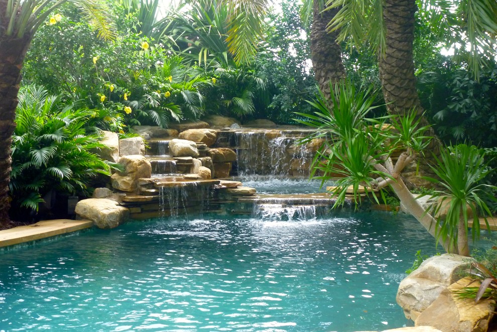 Design ideas for a tropical backyard natural pool in Miami with a water feature.