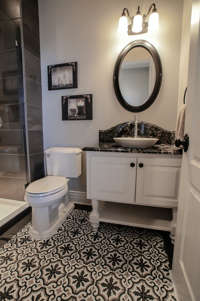 Photo of a mid-sized traditional 3/4 bathroom in Omaha with raised-panel cabinets, white cabinets, an alcove shower, a two-piece toilet, black tile, ceramic tile, grey walls, ceramic floors, a vessel sink, granite benchtops, multi-coloured floor, a hinged shower door and black benchtops.
