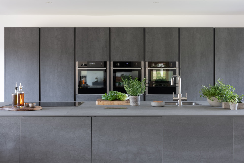 Example of a large minimalist ceramic tile and black floor eat-in kitchen design in Oxfordshire with a double-bowl sink, flat-panel cabinets, gray cabinets, paneled appliances and an island