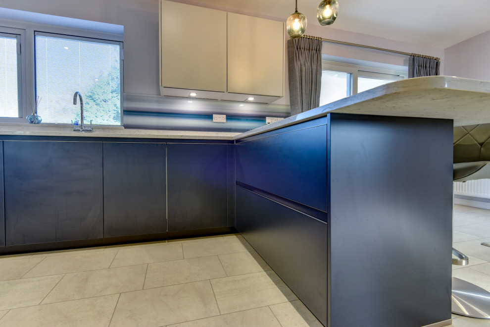 Modern inredning av ett stort vit vitt kök, med en undermonterad diskho, släta luckor, blå skåp, bänkskiva i kvartsit, blått stänkskydd, glaspanel som stänkskydd, svarta vitvaror, vinylgolv, en halv köksö och vitt golv