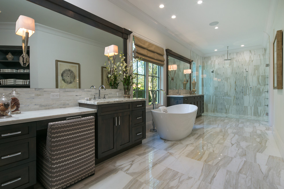 Photo of a large tropical master bathroom in Miami with shaker cabinets, white cabinets, a freestanding tub, a curbless shower, gray tile, stone tile, white walls, marble floors, an undermount sink and marble benchtops.